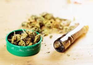 A marijuana 'lid' with a pipe and more cannabis on a wooden surface.