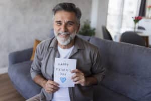 Portrait of a cheerful mature man holding a happy father's day card, celebrating father's day at home