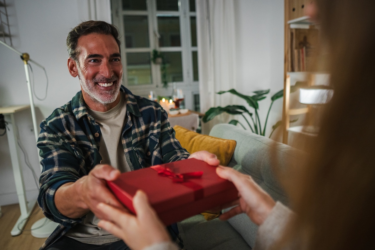 Smiling man receiving a red gift box from another person at home