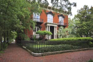 Historic home in Savannah Georgia. Brick sidewalk, brick walls, columns, balconies, palm trees, lush landscaping. This is the elegant Mercer Williams House on Monterey Square in the Historic District of Savannah, Georgia.