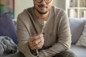 Asian man holding a cannabis joint in a living room, in gesture of sharing
